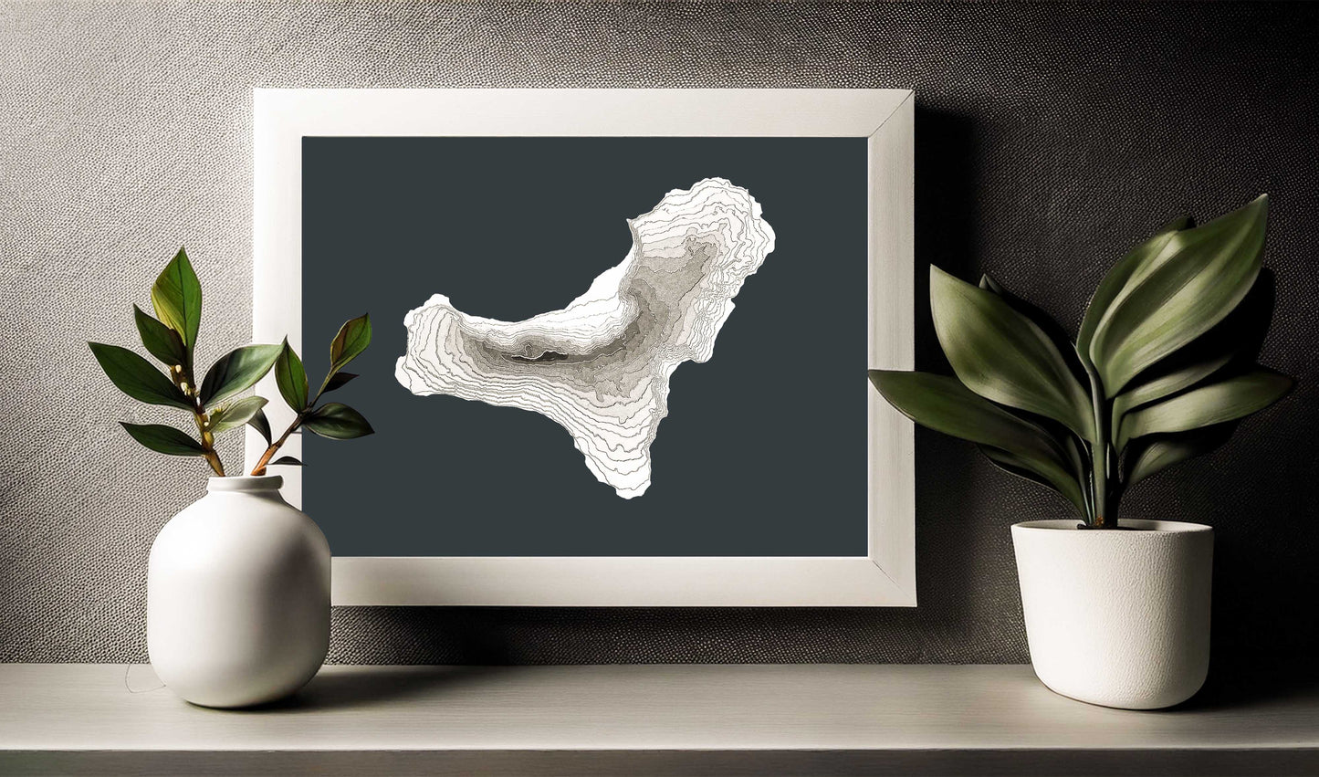This is an image of the raised relief 3d map of El Hierro island in a white wooden frame slightly above a shelf. Although the map is sold unframed it will look good in most kind of frames due to its greyscale colour palette.