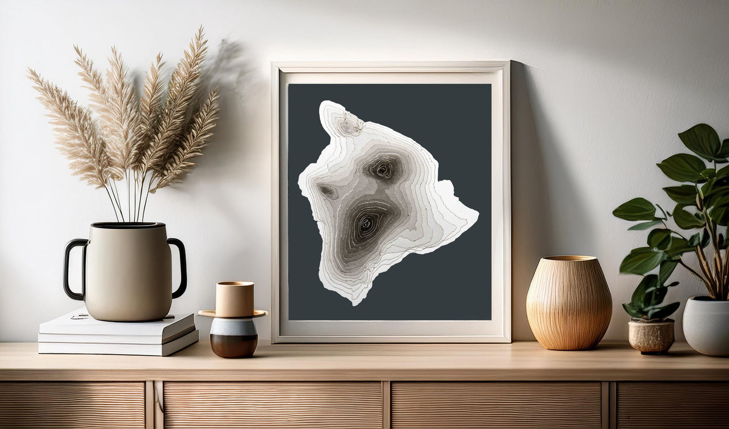 A map of Hawaii, Big Island. Created with layers of cardstock, the unique 3D texture will look great in any home decor. In this image the map is sitting on top of a mid century modern console and leaning against the wall. Thanks to its greyscale colour palette, the map will fit nicely in any kind of home or office style.